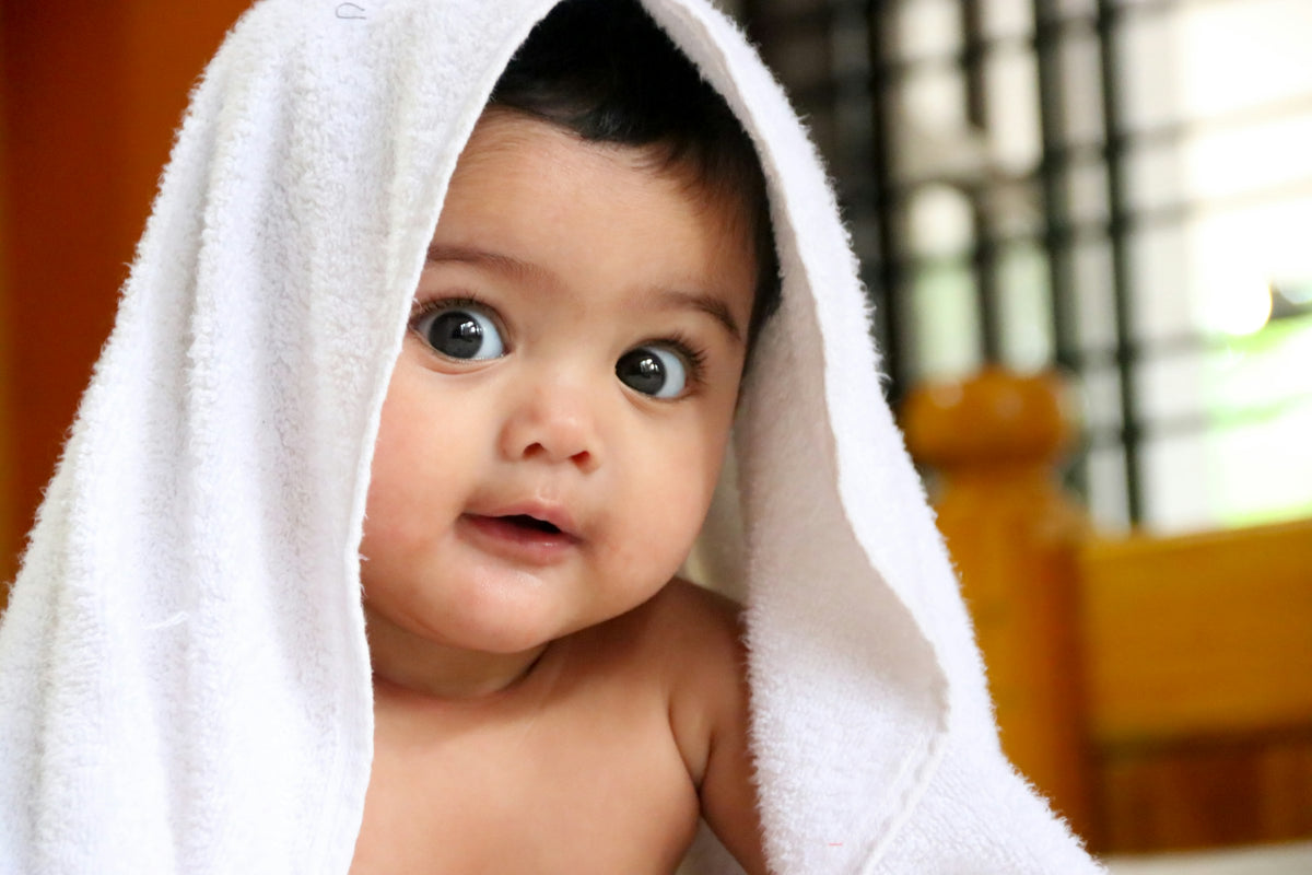 A smiling baby wrapped in a soft white hooded towel after a bath