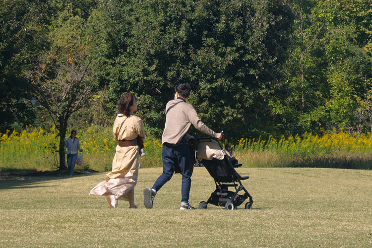 Two parents walking through a park with a baby in a stroller