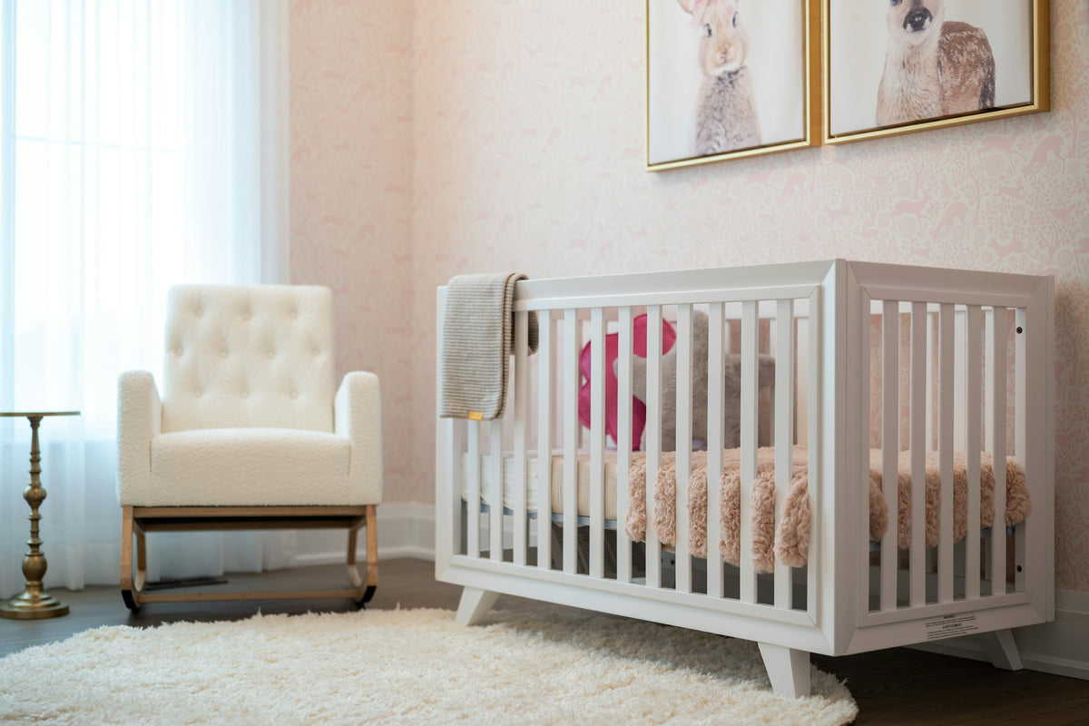 A bright nursery with a white crib, rocking chair and framed wall art